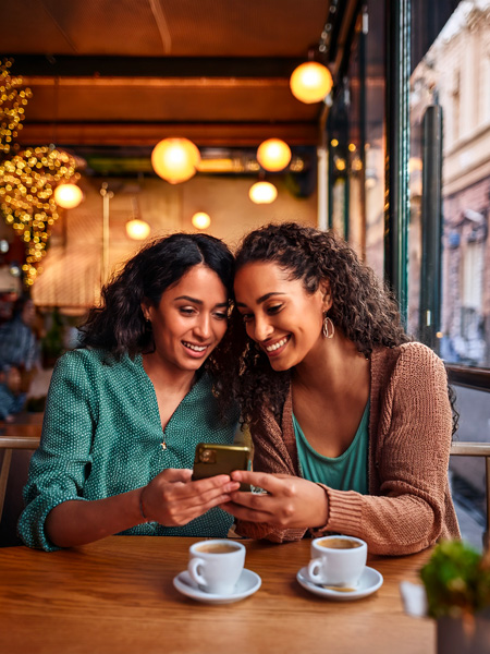 Jeunes femmes échangeant des sms dans un café - contact greenshelf